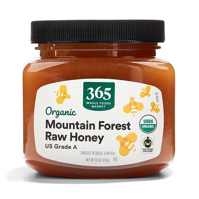 A jar of 365 Whole Foods Market Organic Mountain Forest Raw Honey with a clear label showing the USDA Organic and Fair Trade Certified logos. The honey is described as US Grade A, with the product origins listed as Brazil and Mexico
